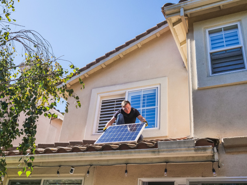 Mann der auf einem Haus Solarpanele instaliert